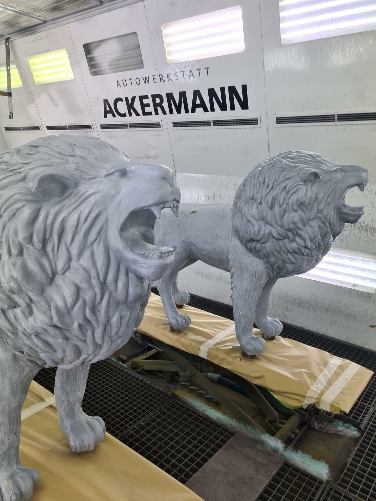 Zwei graue Löwenstatuen in der Lackierkabine der Autowerkstatt Ackermann, während der Neulackierung.