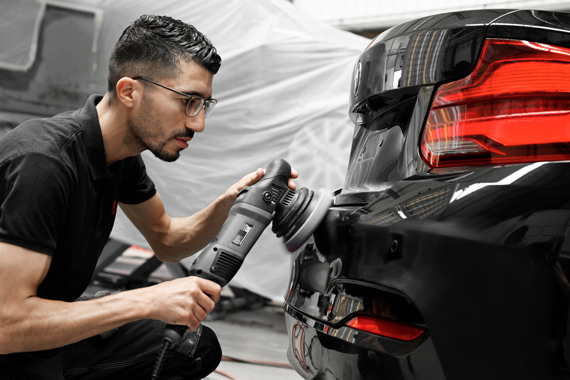 Ein Mitarbeiter von Autowerkstatt Ackermann poliert die Heckpartie eines schwarzen Autos mit einem Poliergerät in der Werkstatt.