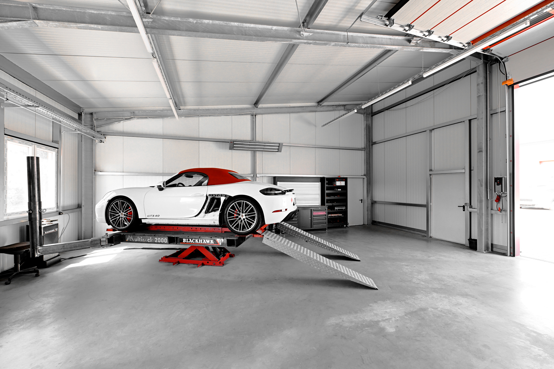 Ein weißer Porsche mit rotem Verdeck steht auf einem Blackhawk Multitrack 2000-Aufzug in der modernen Werkstatt von Autowerkstatt Ackermann in Merenberg-Allendorf.