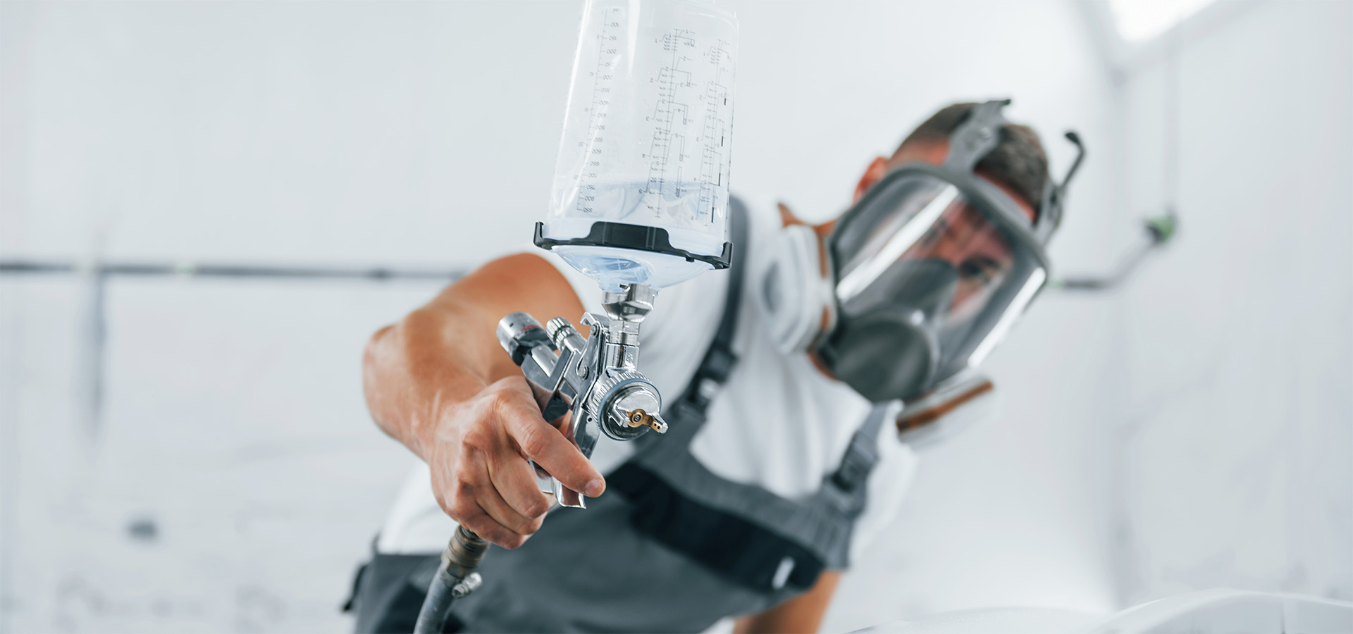 Lackierer mit Schutzmaske bedient eine Spritzpistole zur Fahrzeuglackierung in der Werkstatt von Autowerkstatt Ackermann, einem KFZ-Fachbetrieb mit umfassenden Werkstattleistungen.