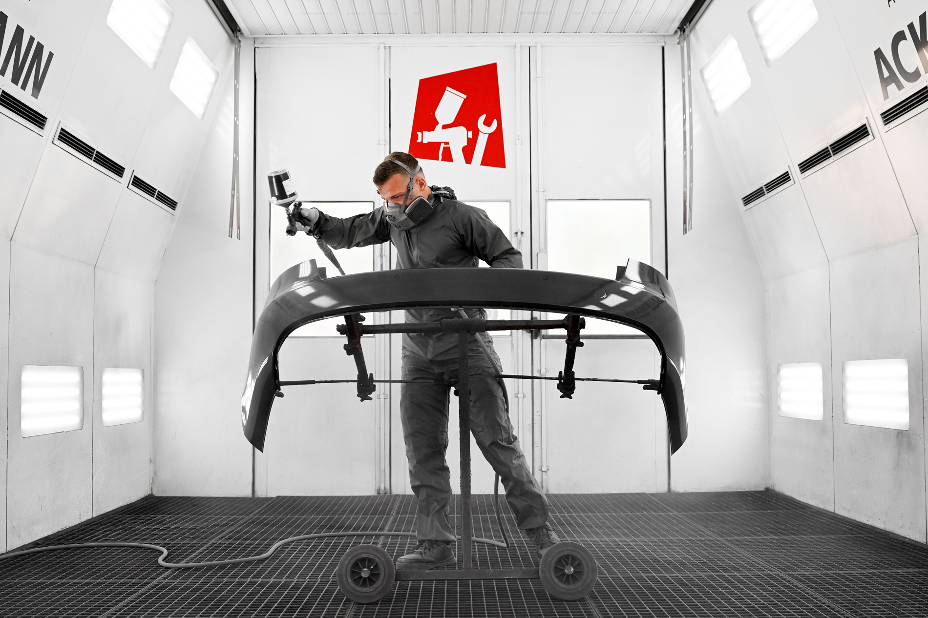 Mitarbeiter der Autowerkstatt Ackermann lackiert ein Autoteil in der Lackierkabine – Fachwerkstatt für KFZ-Reparaturen, Lackierung und Unfallinstandsetzung.