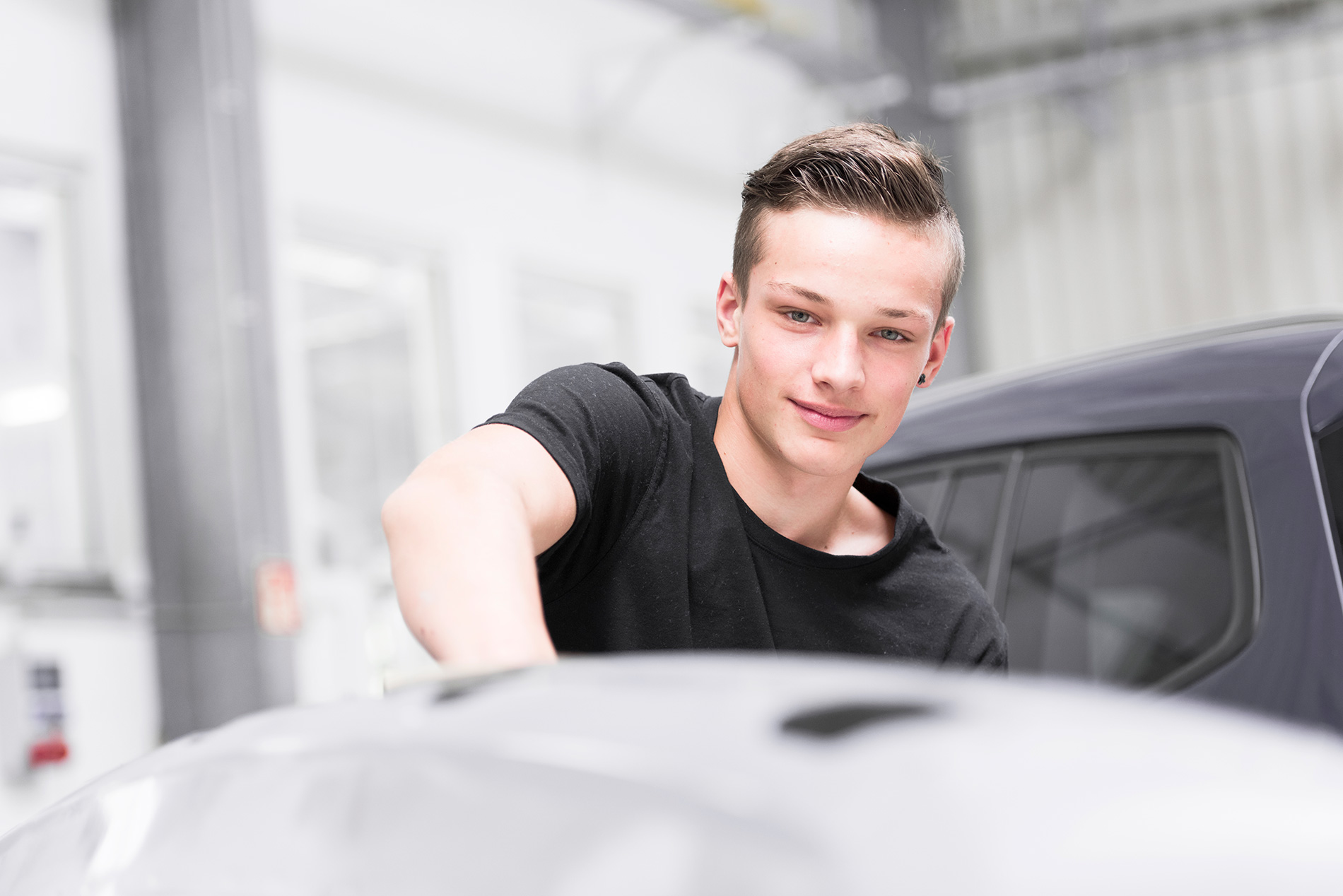 Ein junger Mechaniker in schwarzem T-Shirt arbeitet an einem Fahrzeug in der Werkstatt von Autowerkstatt Ackermann, einem breit aufgestellten KFZ-Fachbetrieb mit Werkstattservice, Lackiererei und Unfallinstandsetzung.