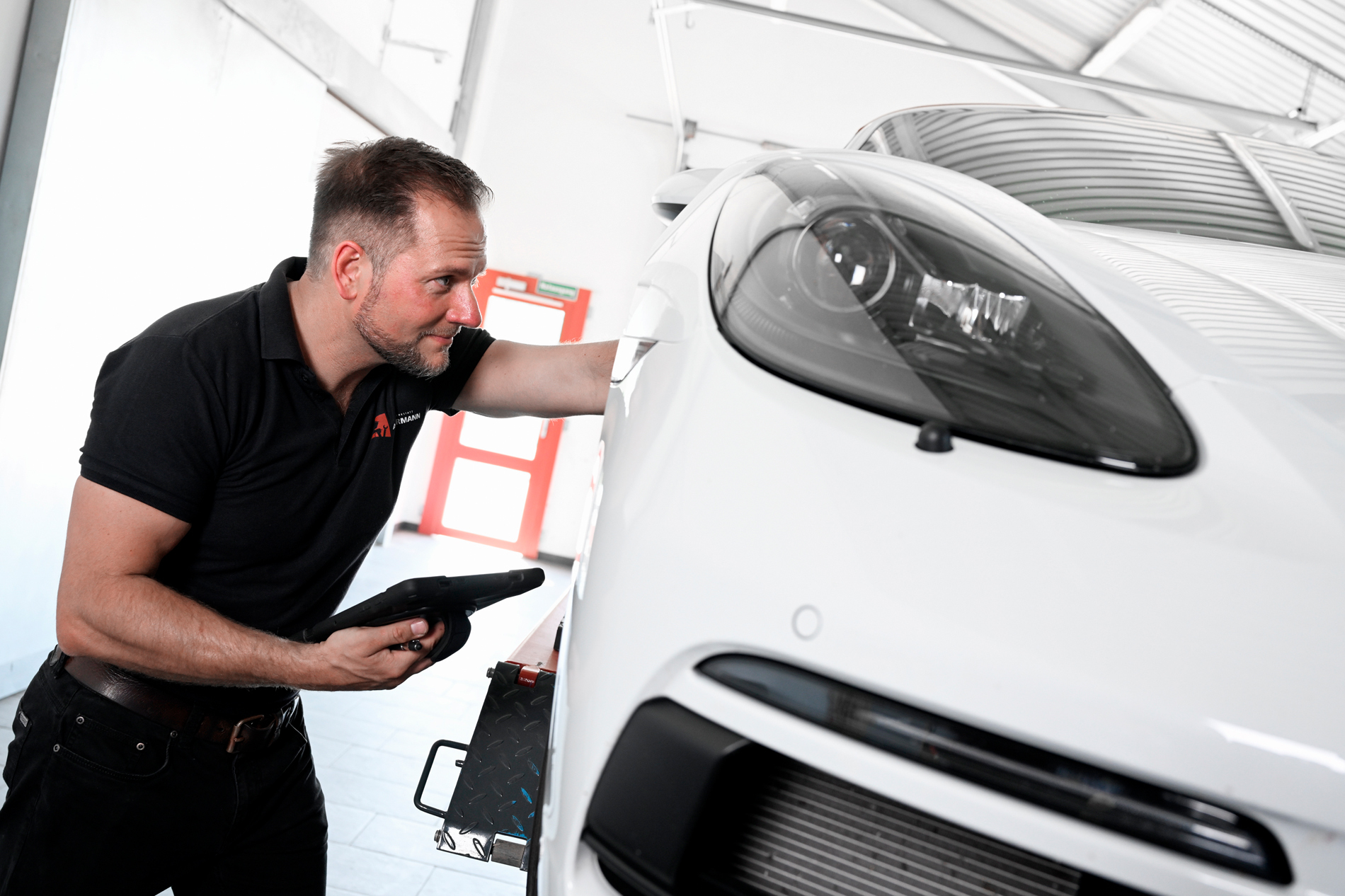 Mechaniker des KFZ-Fachbetriebs Autowerkstatt Ackermann in Merenberg-Allendorf prüft ein weißes Fahrzeug mit Tablet im Werkstattservice – Spezialist für Werkstattservice, Lackiererei, Unfallinstandsetzung und Young-/Oldtimer.