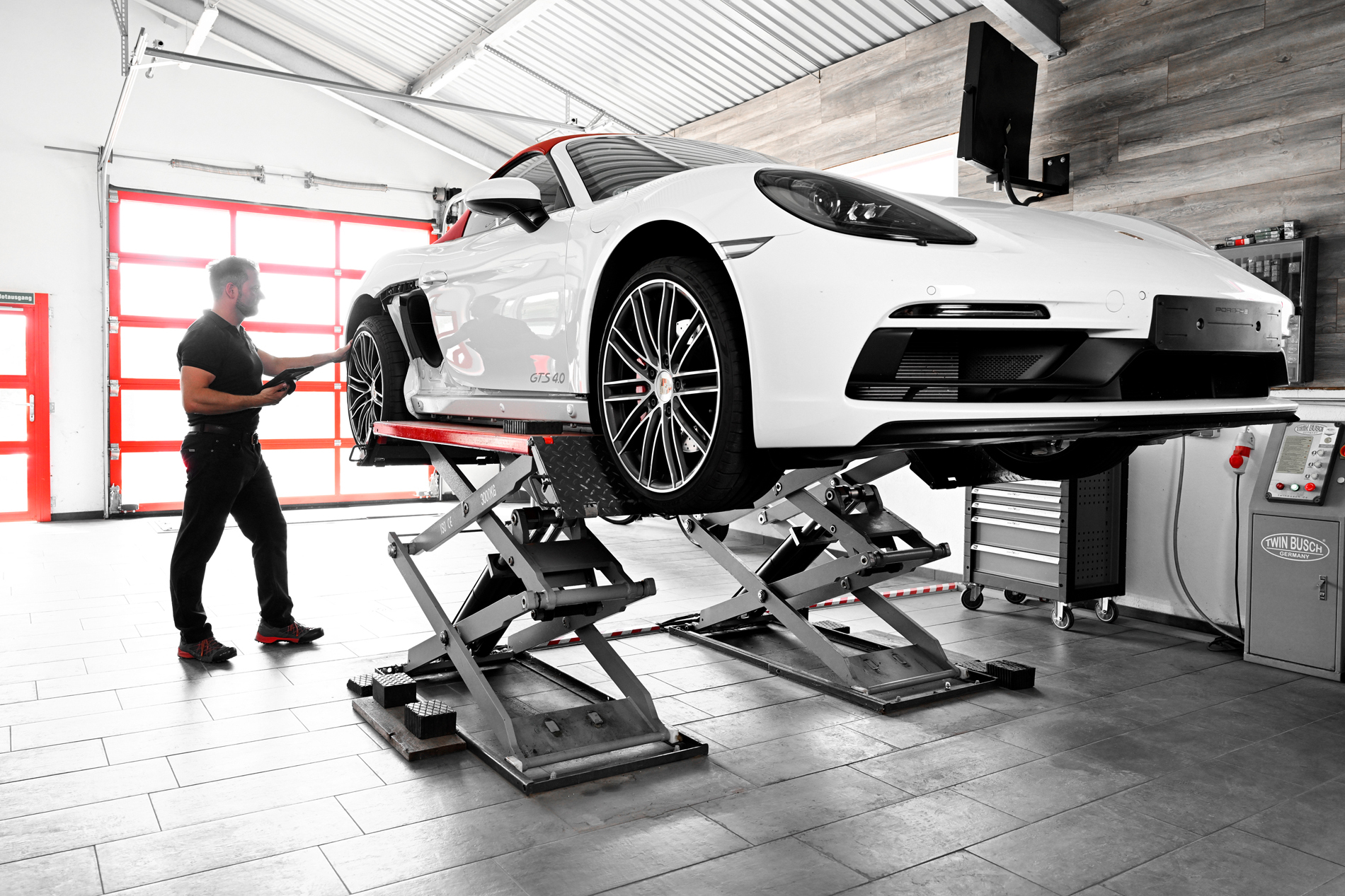 Ein weißer Porsche wird in der Autowerkstatt Ackermann auf einer Hebebühne gewartet, während ein Mechaniker die Arbeiten durchführt.