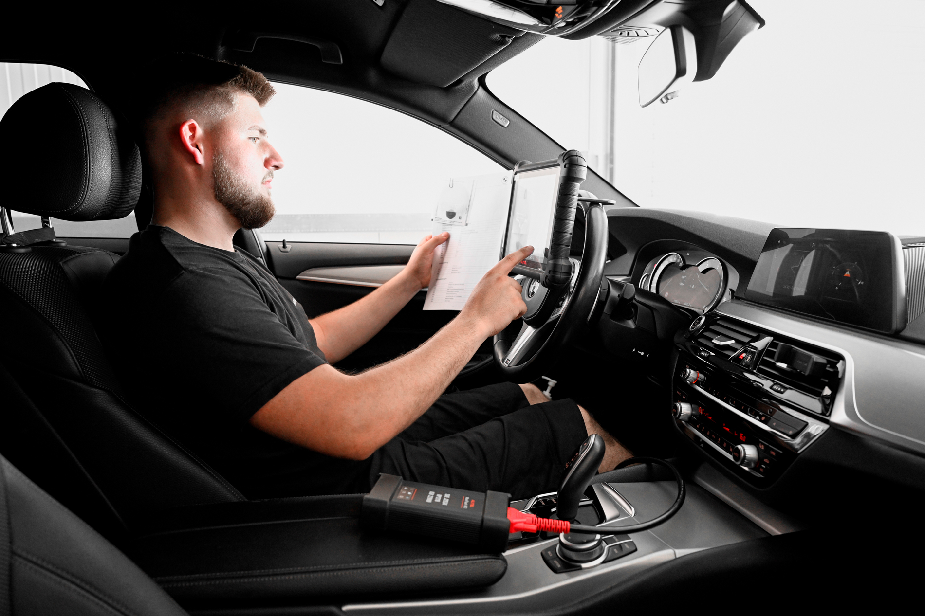 Ein Mechaniker in einem PKW nutzt ein Diagnosegerät zur Fahrzeugdiagnose, hält dabei einen Zettel – typische Tätigkeit in der KFZ-Fachwerkstatt Autowerkstatt Ackermann.