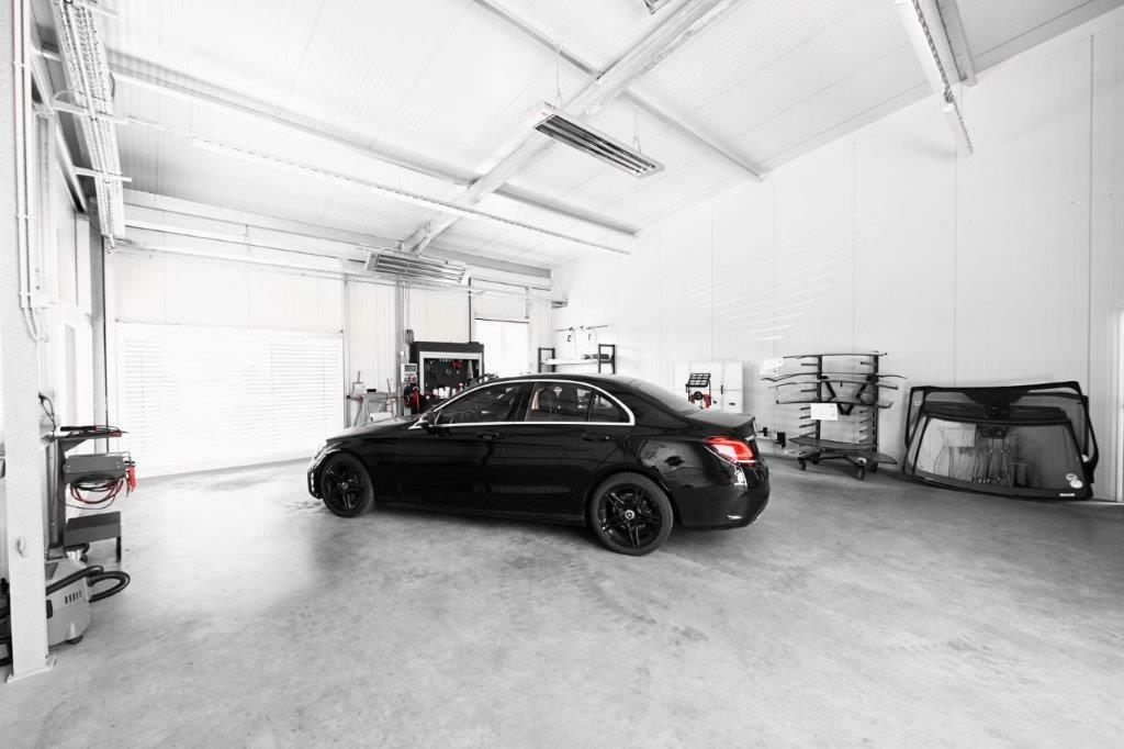 Innenaufnahme einer sauberen Autowerkstatt mit einem schwarzen Pkw, Werkstattausrüstung und einem Autoglas, die die fachgerechten Dienstleistungen von Autowerkstatt Ackermann in Merenberg-Allendorf repräsentiert.
